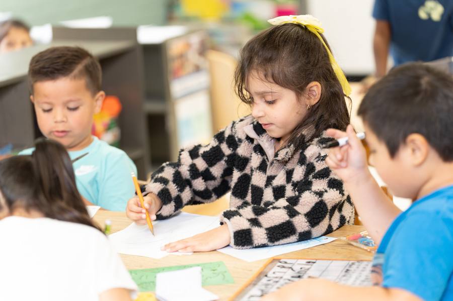 A student writing at her desk during a Community Preschools classroom activity